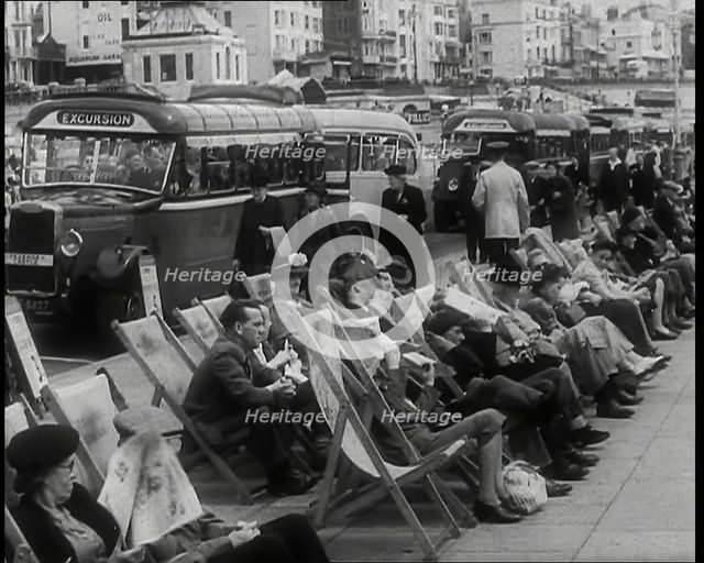 Men and Women Sitting in Deckchairs on the Promenade at  Brighton With a Row of Buses..., 1939. Creator: British Pathe Ltd.