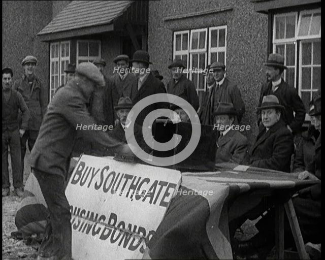 Men Buying Housing Bonds in Southgate. They Take a Piece of Paper from a Box on the Table..., 1921. Creator: British Pathe Ltd.