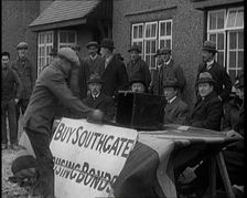 Men Buying Housing Bonds in Southgate. They Take a Piece of Paper from a Box on the Table..., 1921. Creator: British Pathe Ltd