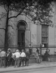 Men standing or sitting in front of the former Bank of Louisiana, 334 Royal Street..., c1920-1926. Creator: Arnold Genthe