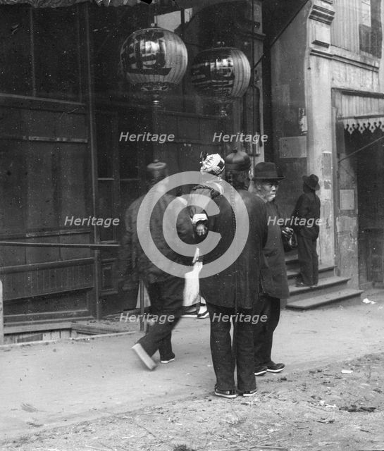 Men standing or walking down a sidewalk, Chinatown, San Francisco, between 1896 and 1906. Creator: Arnold Genthe.