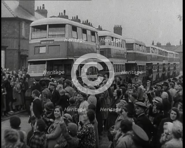 Men, Women, and Children Standing by a Line of Buses Parked in a Residential Street, 1939. Creator: British Pathe Ltd.