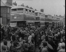 Men, Women, and Children Standing by a Line of Buses Parked in a Residential Street, 1939. Creator: British Pathe Ltd
