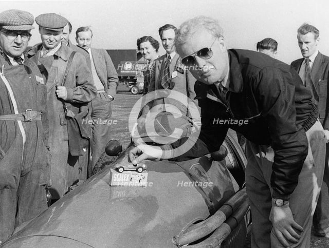 Mike Hawthorn admiring a toy model Ferrari on his racing Ferrari. Creator: Unknown.