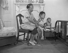 Mrs. Ella Watson, a government charwoman dressing her grandchildren, Washington, D.C., 1942. Creator: Gordon Parks