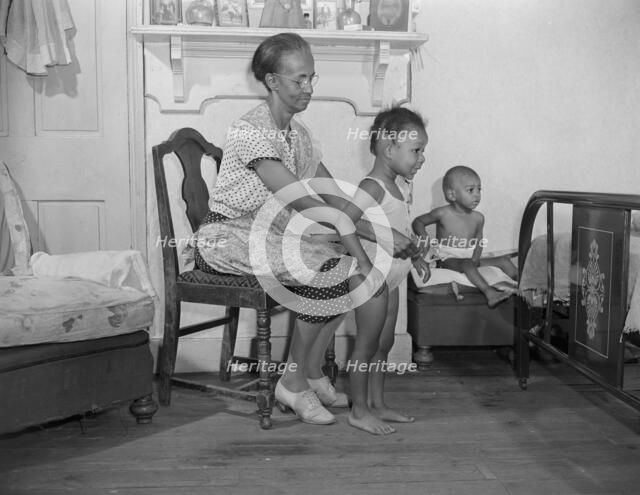 Mrs. Ella Watson, a government charwoman dressing her grandchildren, Washington, D.C., 1942. Creator: Gordon Parks.