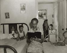 Mrs. Ella Watson, a government charwoman, reading the Bible to her household, Washington, DC, 1942. Creator: Gordon Parks