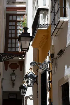 Narrow street with old lamps and balconies in the pedestrian area of Seville, Spain, 2023. Creator: Ethel Davies