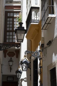 Narrow street with old lamps and balconies in the pedestrian area of Seville, Spain, 2023. Creator: Ethel Davies