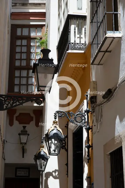 Narrow street with old lamps and balconies in the pedestrian area of Seville, Spain, 2023. Creator: Ethel Davies.