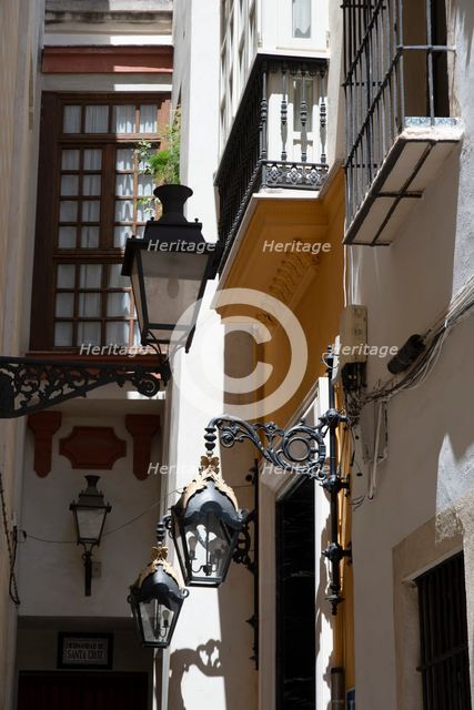 Narrow street with old lamps and balconies in the pedestrian area of Seville, Spain, 2023. Creator: Ethel Davies.