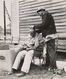Negro getting a haircut in front of church which houses flood refugees. Sikeston, Missouri, 1937-02. Creators: Farm Security Administration, Russell Lee
