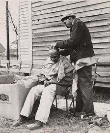 Negro getting a haircut in front of church which houses flood refugees. Sikeston, Missouri, 1937-02. Creators: Farm Security Administration, Russell Lee