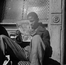 Negro youth reading a funny paper on a door step in the Southwest section, Washington, D.C., 1942. Creator: Gordon Parks