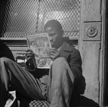 Negro youth reading a funny paper on a door step in the Southwest section, Washington, D.C., 1942. Creator: Gordon Parks