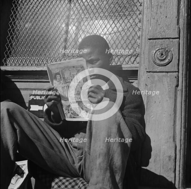 Negro youth reading a funny paper on a door step in the Southwest section, Washington, D.C., 1942. Creator: Gordon Parks.