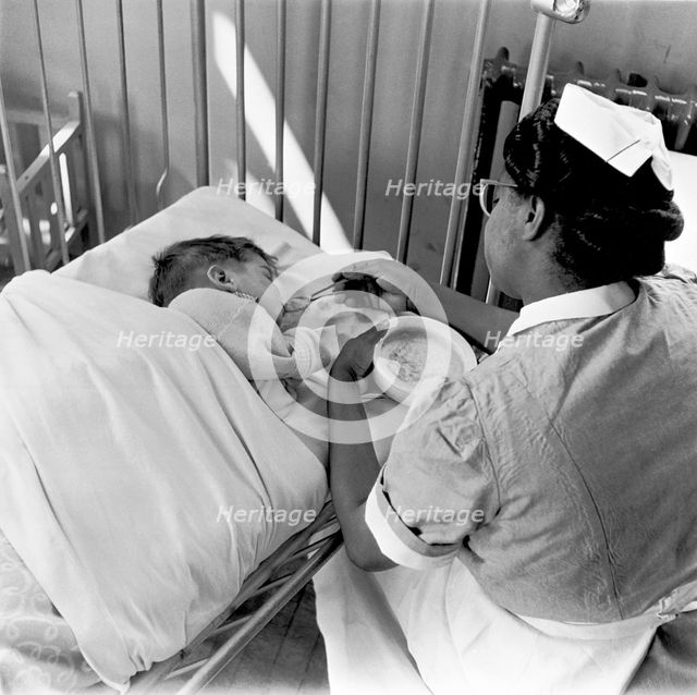 Nurse feeding a child, London, (1960s?). Creator: Henry Grant.