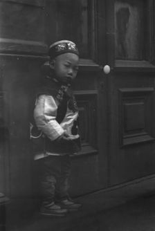 Small boy standing in front of a door, Chinatown, San Francisco, between 1896 and 1906. Creator: Arnold Genthe