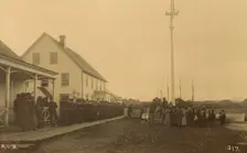 Sailors standing in line on boardwalk with a group of local women and men standing..., 1894 or 1895. Creator: Alfred Lee Broadbent