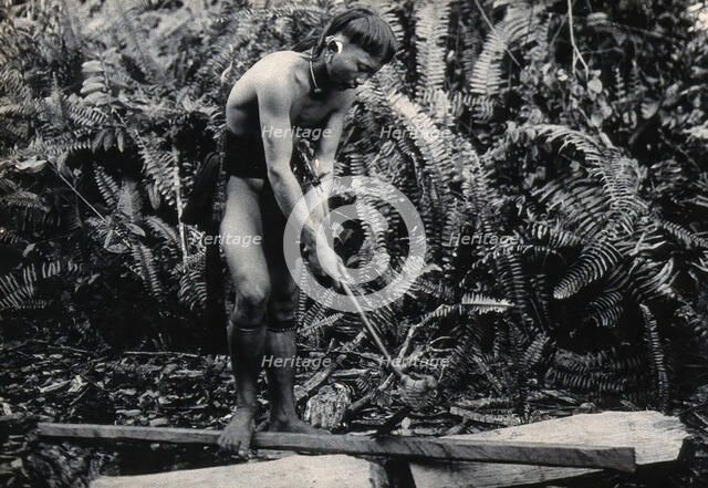 Sarawak: a Kenyah worker cutting a blowpipe from a block of wood, c1900. Creator: Unknown.