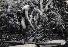 Sarawak: a Kenyah worker cutting a blowpipe from a block of wood, c1900. Creator: Unknown