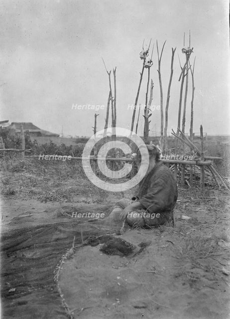 Seated Ainu man working on fishing nets, 1908. Creator: Arnold Genthe.