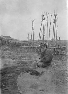 Seated Ainu man working on fishing nets, 1908. Creator: Arnold Genthe