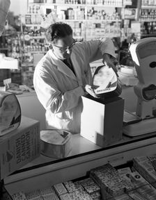 Shopkeeper unpacking canned gammon joints, Mexborough, South Yorkshire, 1963. Creator: Michael Walters