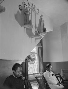 Sitting beneath the emblem of the crucifixion of Jesus on Calvary, Washington, D.C., 1942. Creator: Gordon Parks