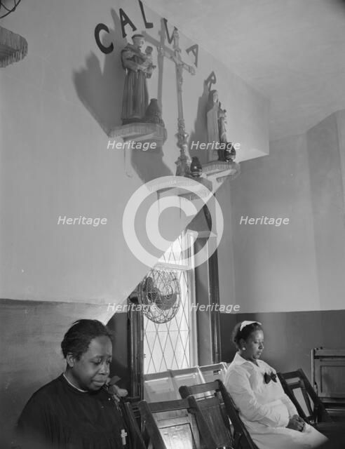 Sitting beneath the emblem of the crucifixion of Jesus on Calvary, Washington, D.C., 1942. Creator: Gordon Parks.