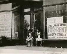 Sidewalk sitters. Two women sitting in doorway of empty storefront that is being..., ca. 1930s. Creator: Unknown