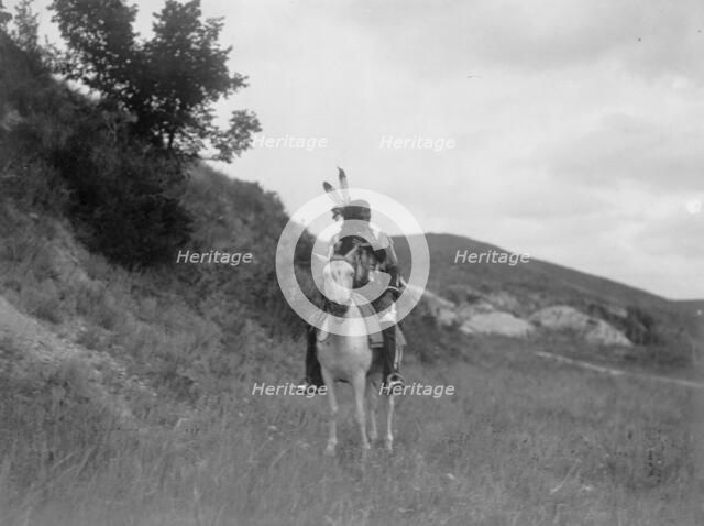 Sioux Indian on horseback, wearing two feathers, beaded buckskin shirt, and leggings..., c1907. Creator: Edward Sheriff Curtis.