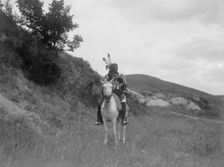 Sioux Indian on horseback, wearing two feathers, beaded buckskin shirt, and leggings..., c1907. Creator: Edward Sheriff Curtis
