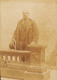 Studio portrait of man dressed in suit and coat, holding bowler hat, c1890. Creator: Steinhardt