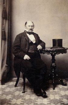 Studio portrait of a man at a table with a top hat, c1865. Creator: Unknown