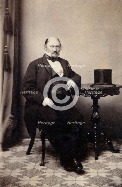 Studio portrait of a man at a table with a top hat, c1865. Creator: Unknown.