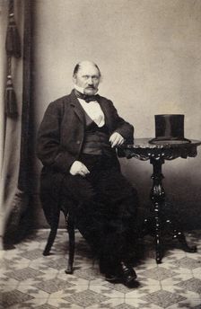 Studio portrait of a man at a table with a top hat, c1865