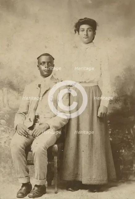 Studio portrait of a young couple, he seated, she with hand on his shoulder, c1900. Creator: Carbon Studio.