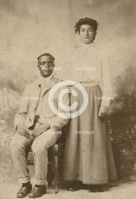 Studio portrait of a young couple, he seated, she with hand on his shoulder, c1900. Creator: Carbon Studio.