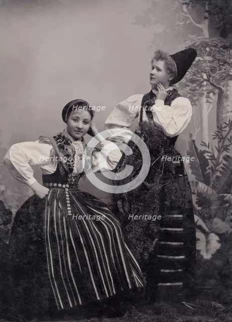 Studio portrait of two young girls posing in folk costumes from Dalarna, 1880-1907. Creator: Helene Edlund.