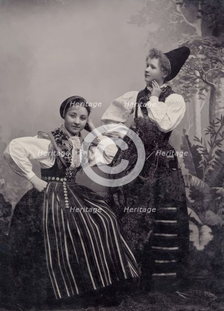 Studio portrait of two young girls posing in folk costumes from Dalarna, 1880-1907. Creator: Helene Edlund.