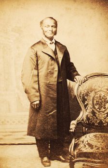 Studio portrait of unidentified man, standing, wearing long coat, c1865. Creator: Sutterley Brothers