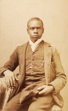 Studio portrait of unidentified seated young man, holding cap, c1880-c1889 . Creator: A. H. Plecker