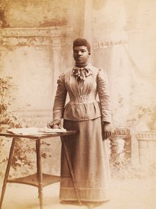 Studio portrait of woman, hand on books spread on table, (1880-1940?). Creator: Madison Art Studio