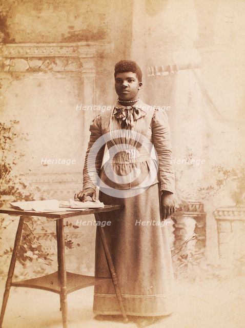 Studio portrait of woman, hand on books spread on table, (1880-1940?). Creator: Madison Art Studio.