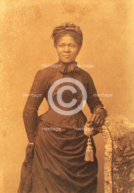 Studio portrait of woman wearing hat and gloves and dress with bustle, c1875. Creator: Unknown.