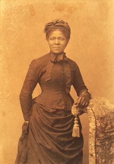 Studio portrait of woman wearing hat and gloves and dress with bustle, c1875. Creator: Unknown