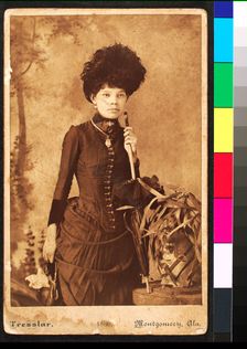 Standing woman, wearing dress with bustle, holding purse at side and umbrella resting..., 1886. Creator: Unknown