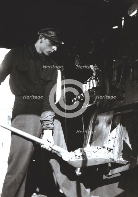 Stoker putting coal to a steam train engine.
