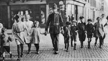 Policeman helping schoolchildren across the road, East End, London, 1926-1927